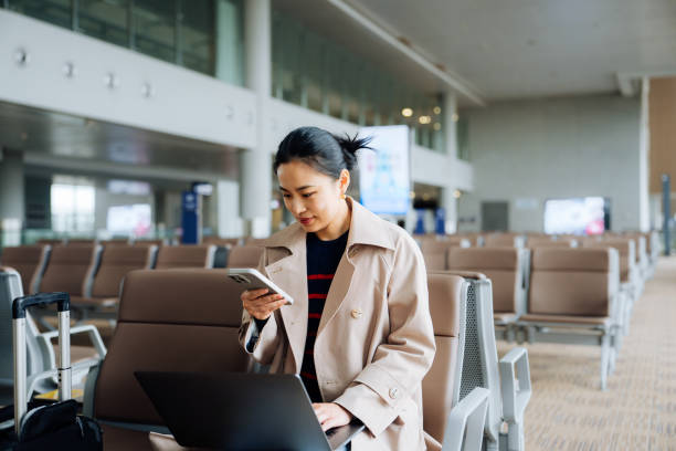 istock Asian young woman wearing trench coat and with suitcase using smartphone while waiting for her flight at airport terminal. Asian businesswoman on business travel. Lifestyle and technology. Business traveller. 2194003302