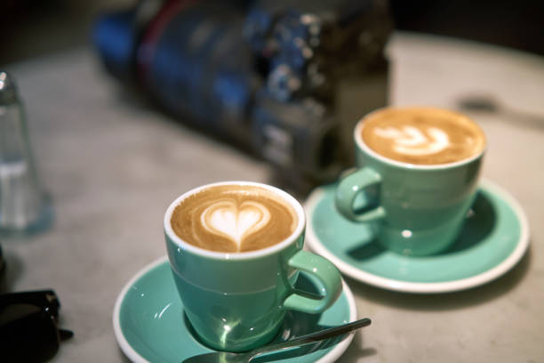 Two cups of cappuccino, one with a heart-shaped latte art, served on a marble table in a cafe, creating a cozy and inviting atmosphere