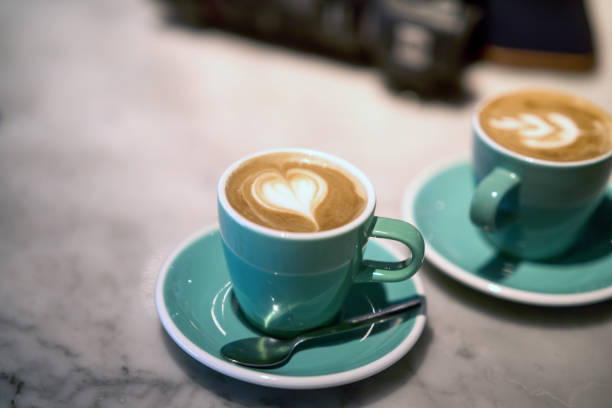 Two cups of cappuccino, one with a heart-shaped latte art, served on a marble table in a cafe, creating a cozy and inviting atmosphere