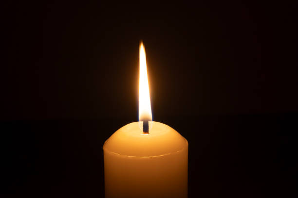 istock A single burning candle flame or light glowing on a big white candle isolated on black or dark background on table in church for Christmas, funeral or memorial service 2194006911