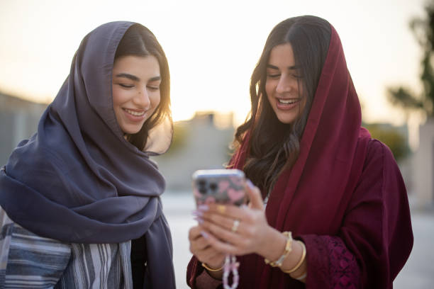 Two Middle Eastern woman friends looking at mobile phone and smiling outside