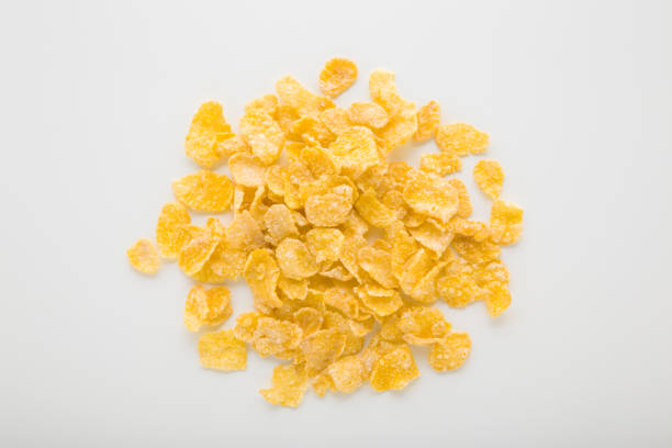 Heap of yellow dry corn flakes on light gray table background. Closeup. Top down view.