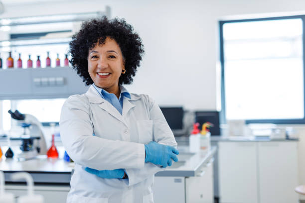 Portrait of a mature female scientist smiling with crossed arms while standing in a modern laboratory, demonstrating confidence and expertise in scientific research