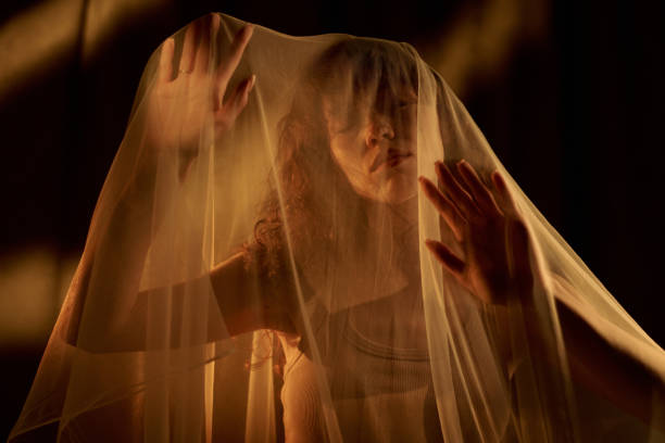 Low angle shot of curly haired young adult woman with closed eyes hiding under veil