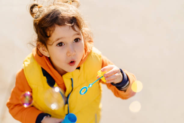 istock Young girl joyfully blowing soap bubbles outdoors during sunny day 2194014327