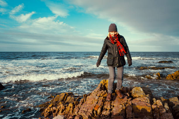 Senior woman walking on the shoreline beside the village of Findochty in the Moray region of Scotland.