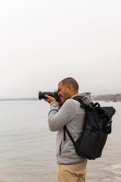 istock A man with a camera is standing on a beach, wearing a backpack 2194017858