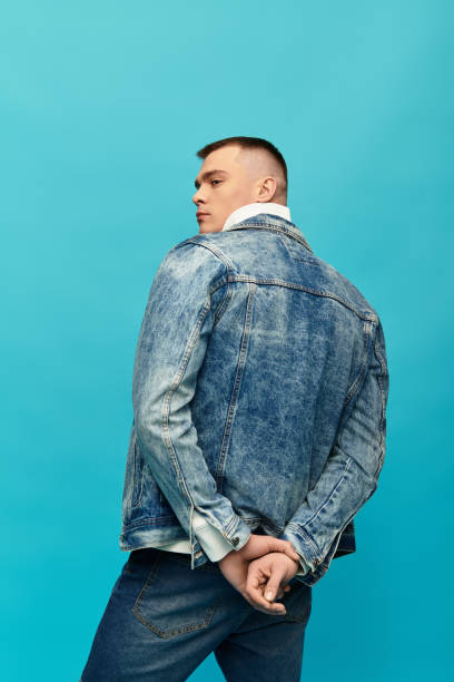 istock Young man in a denim jacket poses against a vibrant turquoise background with confidence 2194020861