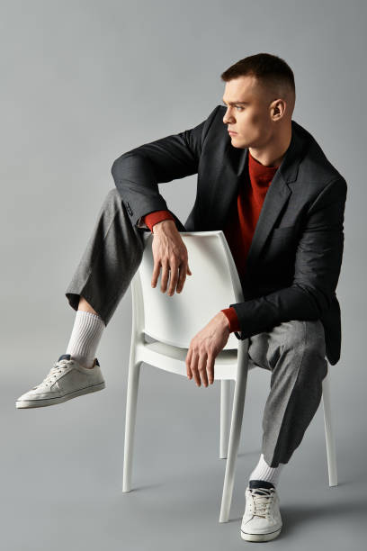 istock Young man in a stylish outfit poses creatively with a chair in a minimalist studio setting 2194022578