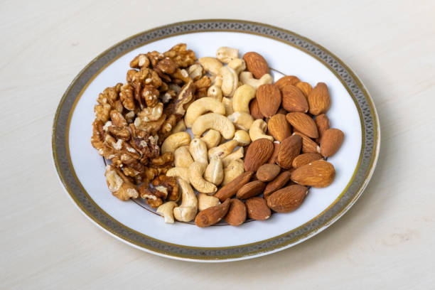 istock Three kinds of nuts  walnuts, cashews, and almonds  served in a white ceramic plate on a light wooden background. 2194022752