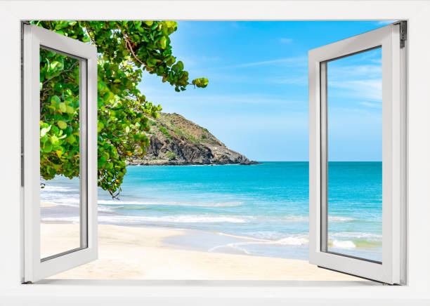 Beach with a white house in the distance. A beach umbrella is on the sand. A window is open to the beach