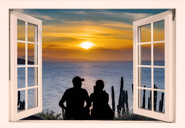 Window with a view of the ocean and a sunset. The curtains are white. The window is open