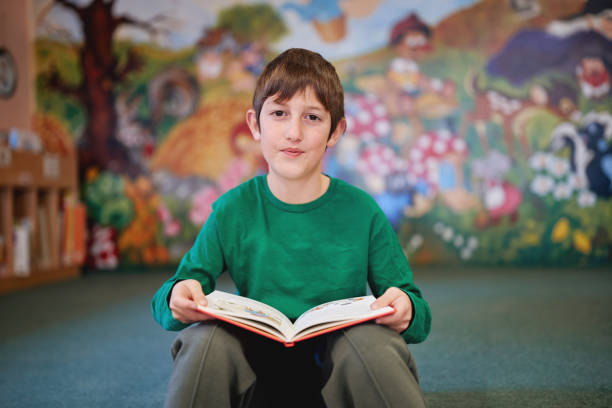 Boy sitting and reading a book in a colorful classroom.