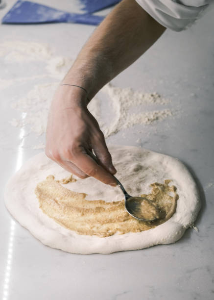 istock Chef Spreading Caramelized Onion Cream on Fresh Pizza Dough by Hand in a Traditional Italian Restaurant Kitchen, Preparing for Gourmet Pizza Creation 2194030906