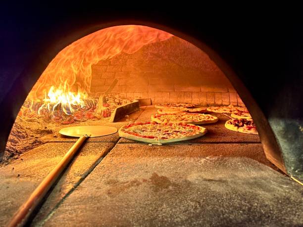 Several pizzas baking in a traditional wood-fired oven, flames dancing and providing the perfect heat for delicious cooking in a charming Venice pizzeria, create an inviting culinary scene