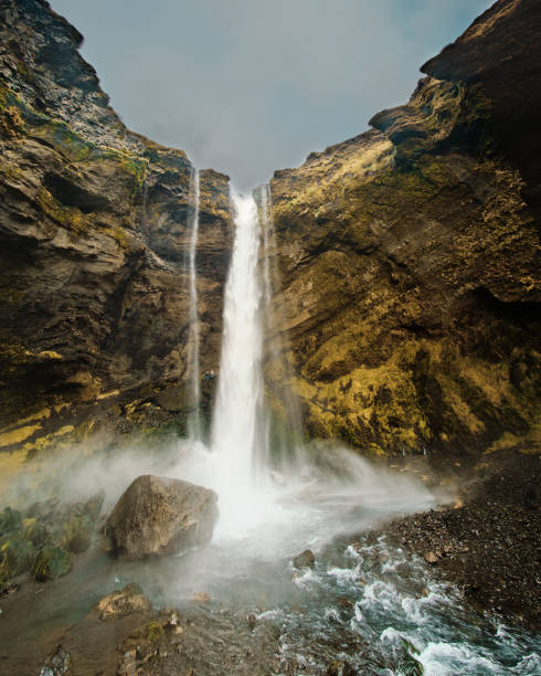Kvernufoss waterfall cascading into a misty pool surrounded by cliffs in South Iceland.