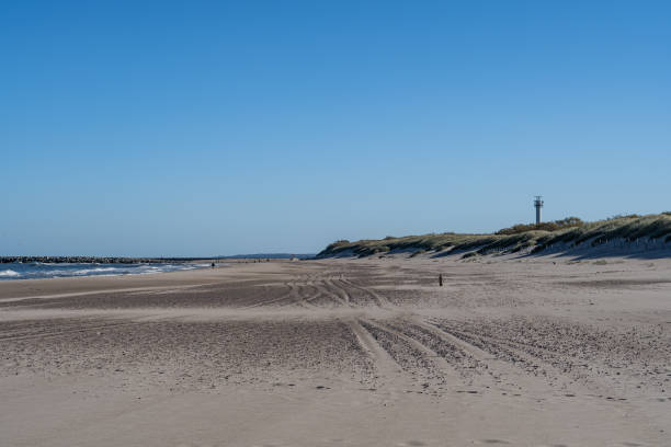 istock Scenic Beach with Sand Dunes and Lighthouse Under Clear Blue Sky 2194038717