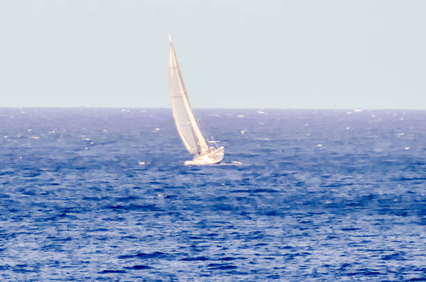 A sailboat is sailing in the ocean. The sky is clear and the water is calm. The sailboat is the only object in the image