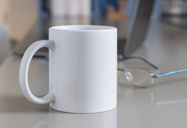 istock White coffee mug on grey office table against opened laptop and glasses closeup, mockup 2194043566