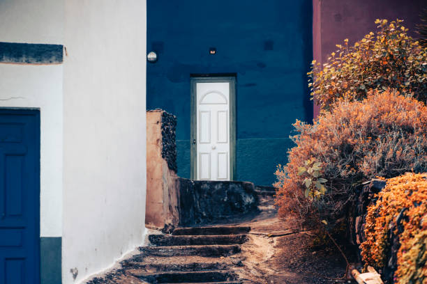 A rustic cozy house with walls painted bright blue and white colors, a view of the window of a vintage-style building, a courtyard with a garden.