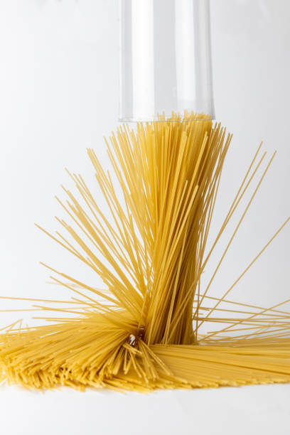 close-up on a white background from the side above the table spaghetti bottom to top spaghetti outside the container stands on the table a cylinder of spaghetti spills over the table