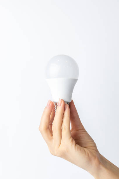 istock close-up on white background from the side, a woman's thin hand holds a white light bulb with a wide base, economical energy consumption, neutral color, lighting element 2194045452