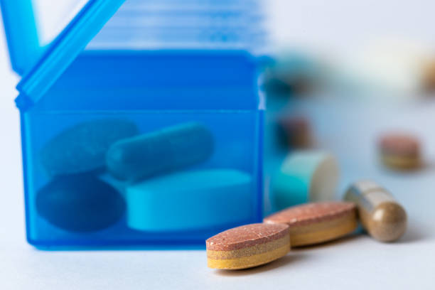 closeup white background two bright blue pill boxes with a couple of open lids for taking pills, health care, partial filling different shapes colors of pills and vitamins pills lie next to the table