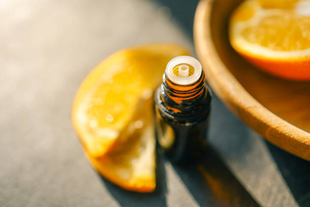 istock Amber glass bottle with open lid on a dark surface, surrounded by fresh orange slices. The warm sunlight enhances the rich tones, creating a natural and refreshing atmosphere 2194046598
