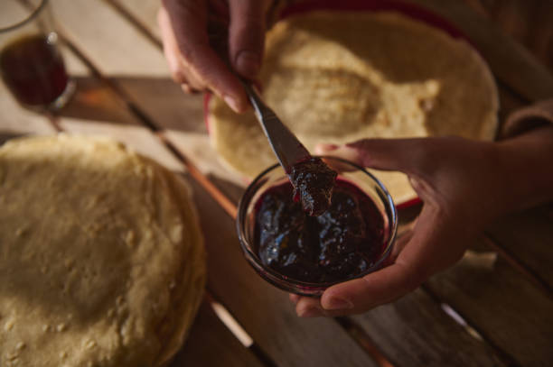 Person spreading jam on crepes with natural light and wooden table setting