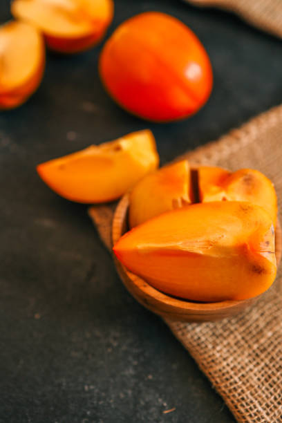istock Rustic composition with fresh persimmons in a wooden bowl and on a dark textured background, accented by burlap. Ideal for seasonal, culinary, and rustic lifestyle themes 2194049196