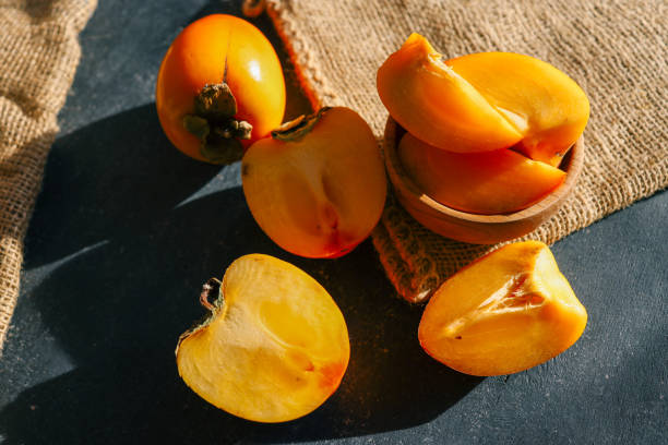 istock Sliced and whole persimmons arranged on a dark textured surface with natural light and burlap, showcasing vibrant colors and rustic simplicity. Perfect for food, seasonal, and healthy living themes 2194049198