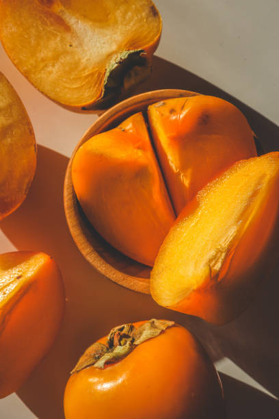 istock Fresh persimmons, both whole and sliced, placed on a rustic burlap cloth over a warm orange background, creating a cozy and autumn-inspired food arrangement 2194049203