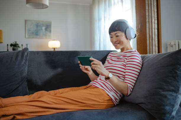istock Woman wearing headphones enjoying content on tablet while relaxing on a couch 2194049475