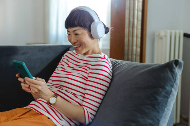istock Happy woman enjoying music while browsing her smartphone on a cozy sofa 2194050015
