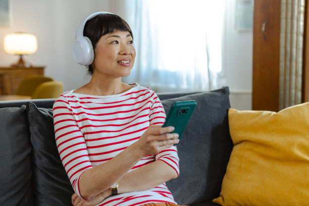 istock Happy woman enjoying music while browsing her smartphone on a cozy sofa 2194050119