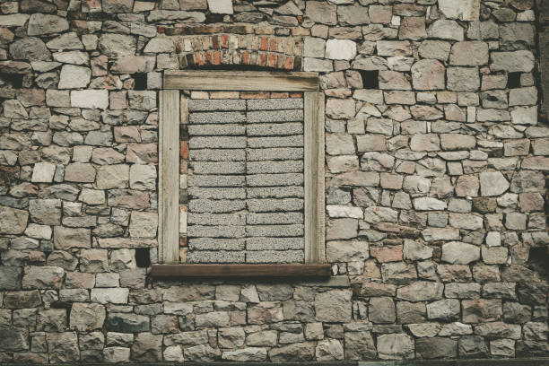 A weathered stone wall features a boarded window, reflecting a sense of abandonment. The textures highlight the passage of time, creating a nostalgic atmosphere in a forgotten location.