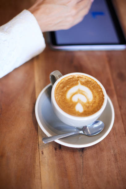 Cappuccino cup on a wooden table next to a digital tablet.