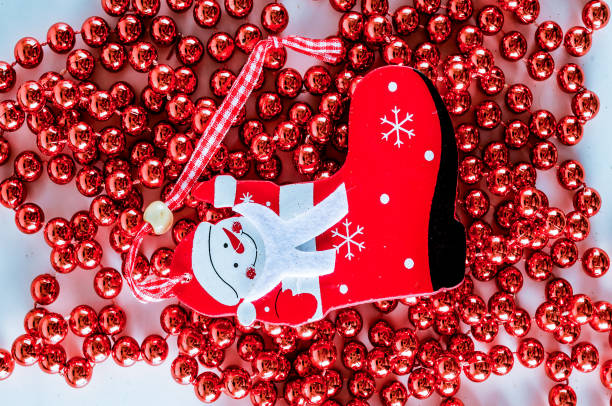 A red christmas ornament with a snowman on it sits on a red string of beads. The ornament is surrounded by a red string of beads, creating a festive and cheerful atmosphere