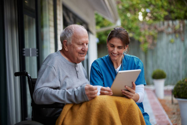 friendly nurse and senior man on wheelchair using digital tablet - ouderenzorg stockfoto's en -beelden