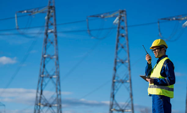istock Technician communicates via radio in high-visibility vest near electrical pylons, under blue sky. 2194055222