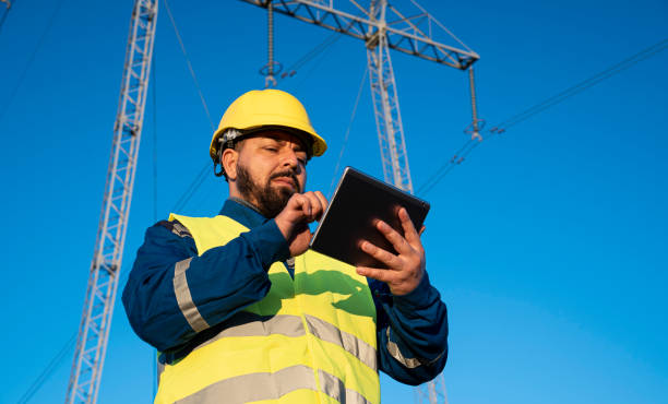 istock Technician communicates via radio in high-visibility vest near electrical pylons, under blue sky. 2194055233