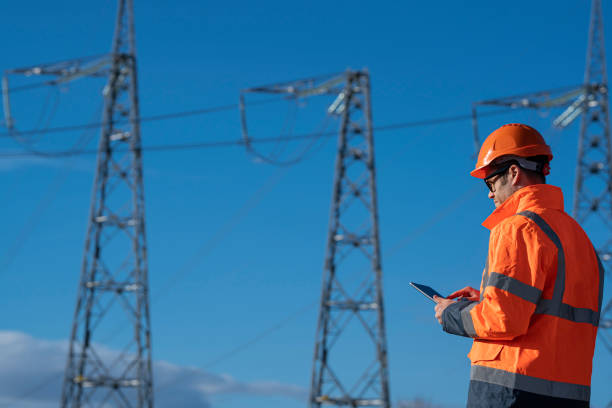 istock Engineer in orange safety gear using tablet near high voltage power lines under blue sky. 2194055273