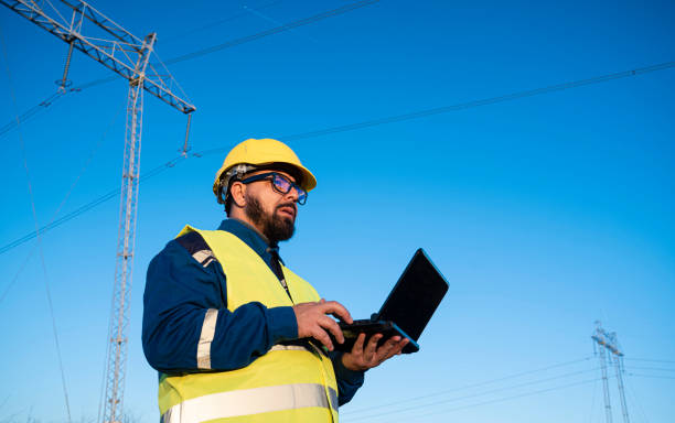 istock Engineer on laptop in safety gear explores data flow at electric station with clear blue sky. 2194055280