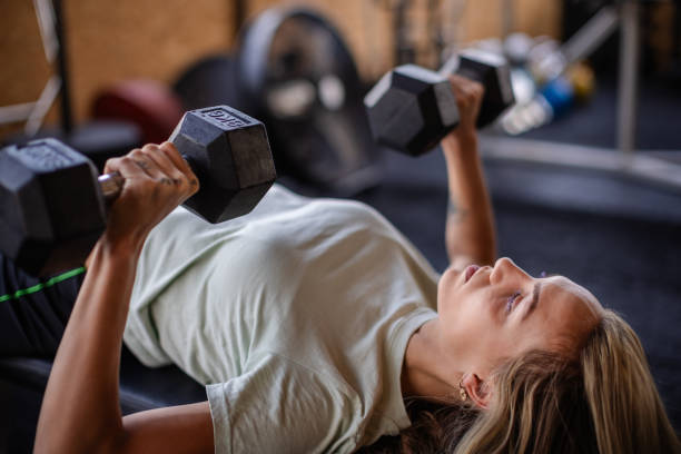 istock Woman lifting dumbbells on bench in bright gym. 2194055999