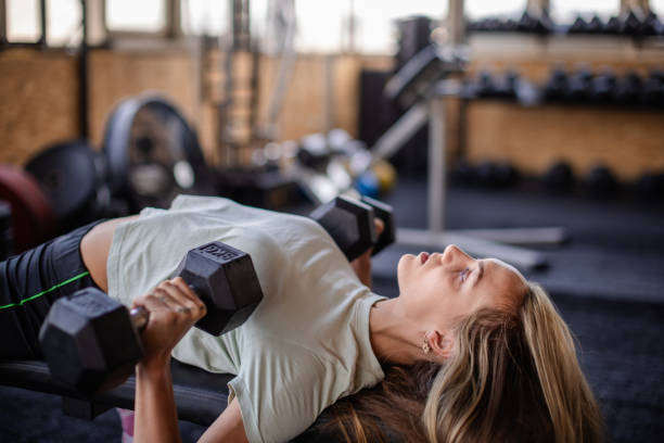 istock Woman lifting dumbbells on bench in gym setting. 2194056035