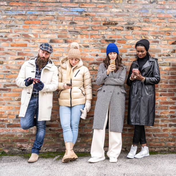 istock Multicultural friends standing against a brick wall, fully absorbed in their smartphones. A colorful urban depiction of technological dependence, apathy, and modern disconnection. 2194056078