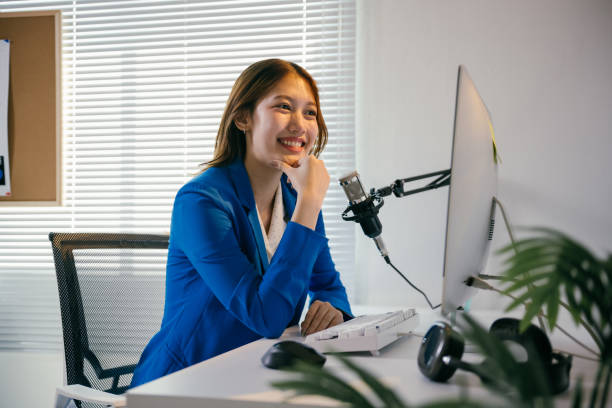 istock Young asian businesswoman smiling while recording a podcast in a modern office, utilizing a professional microphone and computer, creating engaging content in a stylish workspace 2194060129