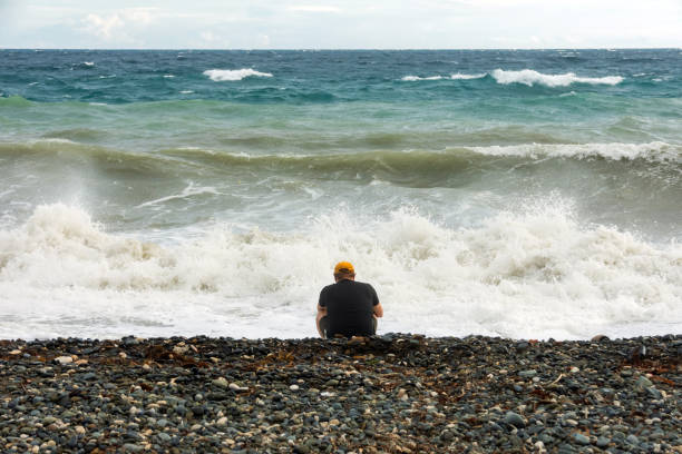 lonely depressed person sitting alone on the ocean shore with raging waves.
