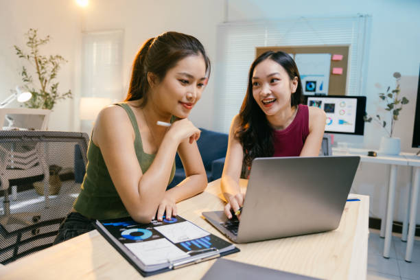 istock Two young asian businesswomen are collaborating on a project, analyzing charts and data on a laptop in a brightly lit modern office, demonstrating teamwork and focus 2194063605