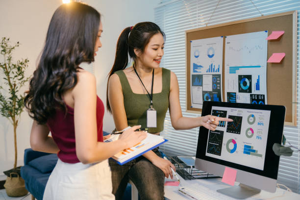 istock Two young asian businesswomen are discussing financial charts displayed on a computer screen, collaborating on data analysis and investment strategies in a modern office setting 2194064438